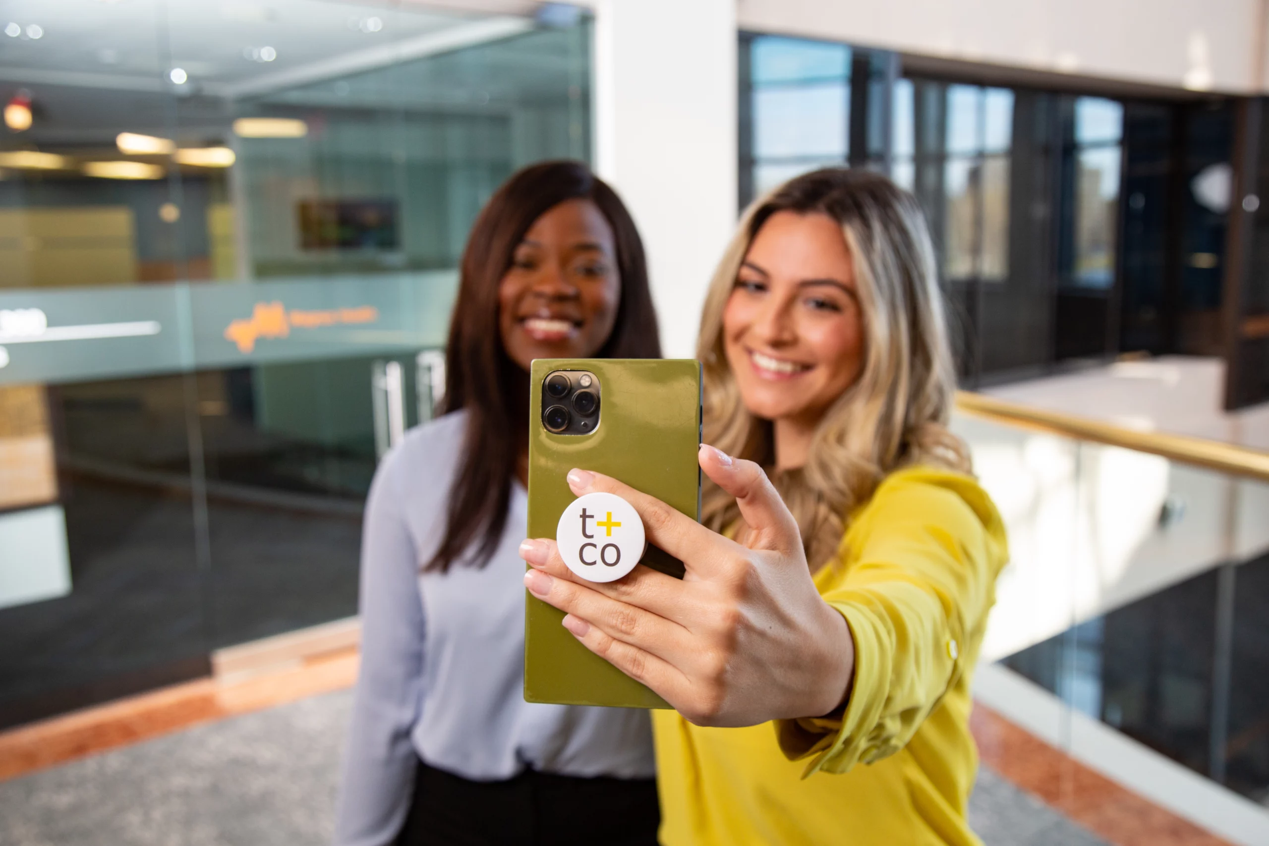 Two employees taking a selfie with a branded Tonneson + Co pop socket on the phone.