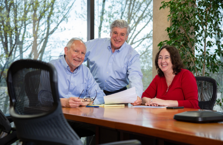 Three employees smile at the camera while at the head of a conference table.