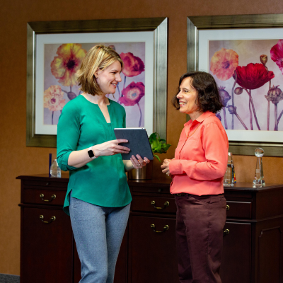 Two accounting professionals stand with an iPad with two large images of flowers on the wall behind them.