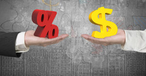 One hand holds a 3D percent sign while another hand holds a 3D dollar sign in font of a gray background with a hand drawn sky line and statistics.