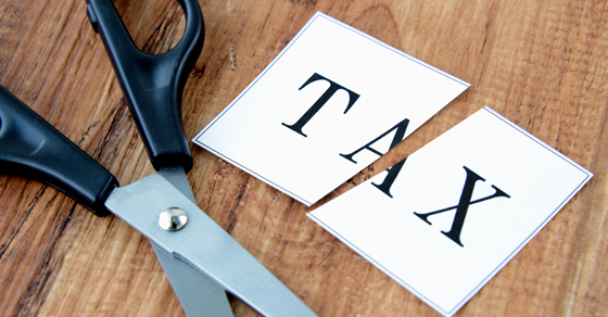 Scissors on a wood table with a piece of paper with the word "Tax" cut in half.