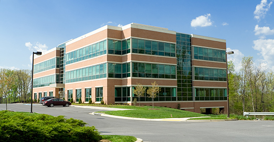 A large brown office building, with many windows, and parking lot on a bright sunny day.