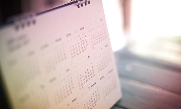 A blurry calendar, with March and July in focus, is placed on a wooden floor.