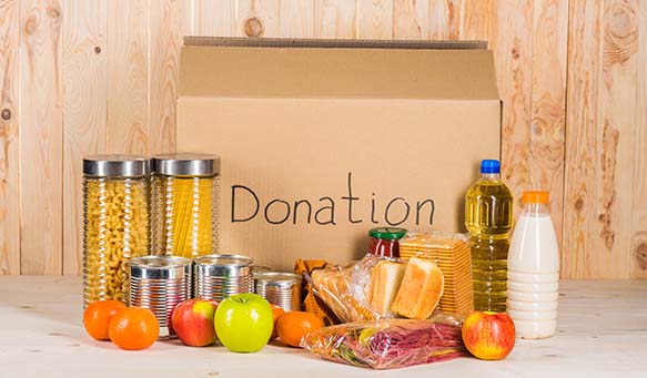 A donation box in front of a wood wall with basic food necessities displayed in front of it.