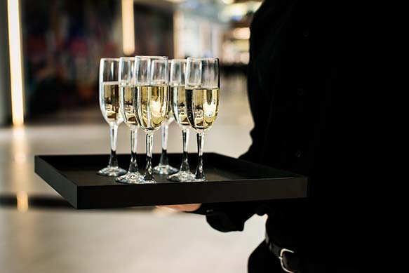 A waiter holds a tray of six champagne bottles.